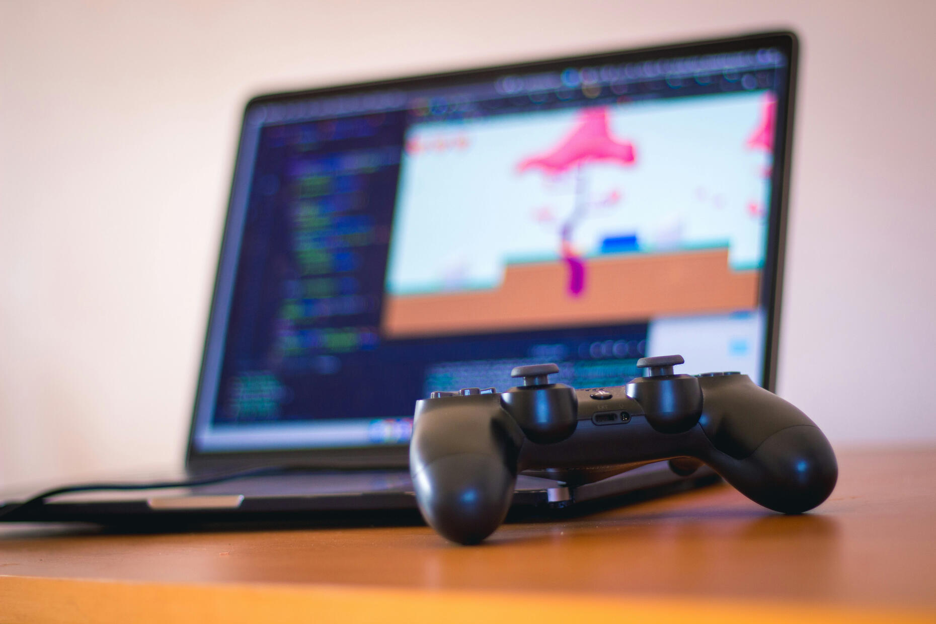 Controller in the front with a blurred laptop with code and a game running